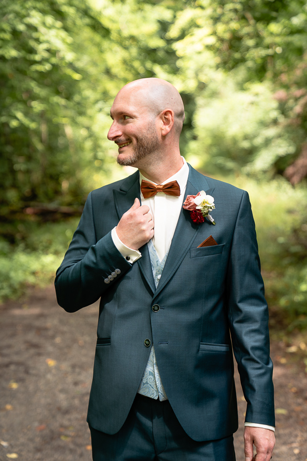 Bräutigam mit Fliege in Petrolfarbenem Anzug steht im Wald - Hochzeit Schmellbachtal