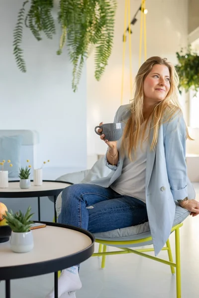 Junge Frau in hellblauem Blazer sitz mit Kaffeetasse in der Hand im Café
